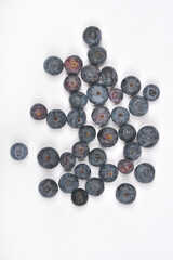 A scattering of fresh, dark blueberries is spread across a plain white background, viewed from directly above