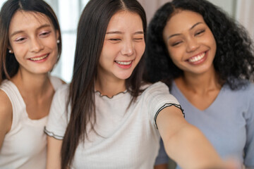 Diverse group of female friends taking selfie with smartphone smiling and posing for social media post, capturing happy and fun moments together, technology, joyful expressions and laughter at home
