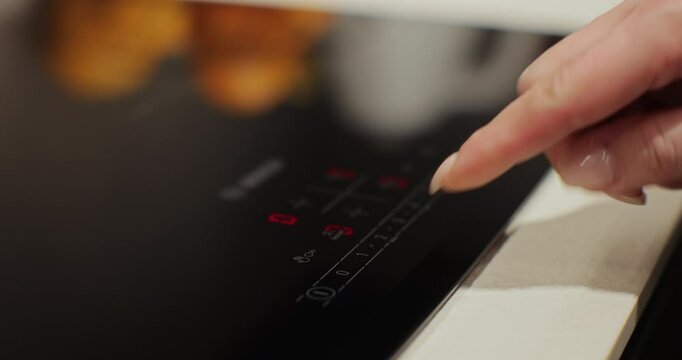 Woman hand turn on induction stove to cook. Finger touching sensor button on induction or electrical hob. Modern technology.