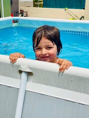 Close-up portrait of a happy Caucasian boy enjoying a sunny summer day in an above-ground pool.