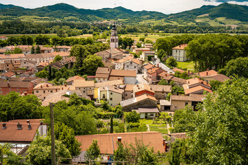Picturesque View Of Vipava From Castle Ruins: Red-Tiled Rooftops And Church Tower Nestled In Green Valley With Blooming Flowers In Foreground And Rolling Fields In Background, Slovenia © Natalia Schuchardt