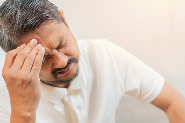 Close-up unhappy Asian man suffering from headache over white background