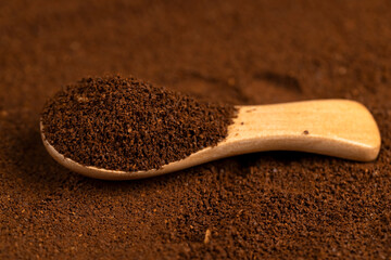 ground coffee and a spoon, a large number of roasted ground coffee beans in powder and a wooden spoon