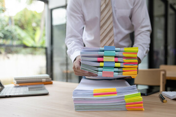 A man is working in an office. On his desk are several sheets of paper, a notebook, a laptop, a calculator, and a pen. The man is staring intently.

