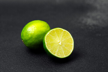 Fresh limes placed on a dark surface with one lime cut in half