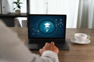 E-learning Platforms person sitting wooden table front of laptop displaying digital education or learning icon with graduation cap and light bulb