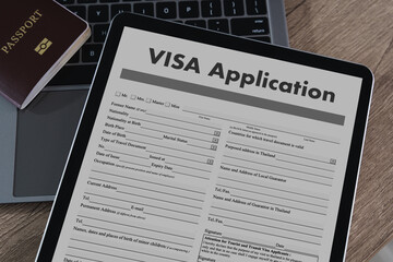 Visa application digital tablet displaying visa application form with passport and laptop background, wooden surface, representing travel