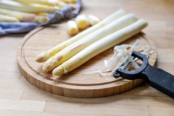 White asparagus is peeled on a wooden cutting board in the kitchen, healthy cooking with seasonal vegetables, copy space, selected focus