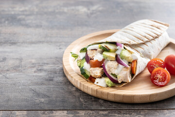 A delicious grilled chicken wrap with vegetables and avocado on wooden table. Copy space