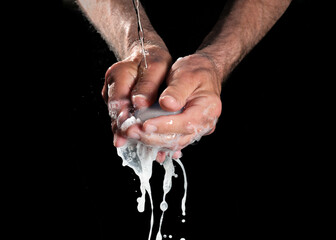 Hands washing themselves under running water with soap and dripping foam against a black background, health and hygiene concept, copy space