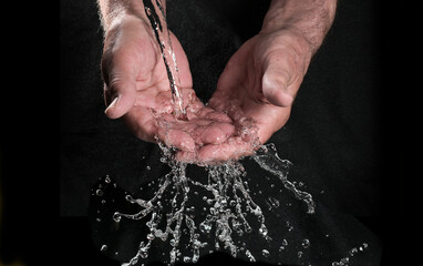 Hands catching running water running with splashing and glittering drops against a black background, concept for environmental resources, health and hygiene, copy space