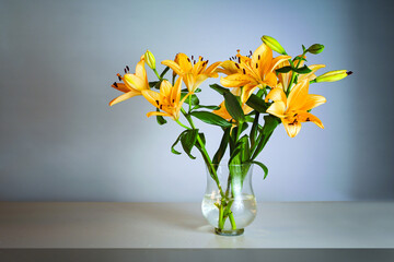 Flower bouquet with orange lilies in a glass vase on a table in front of blue gray background with copy space
