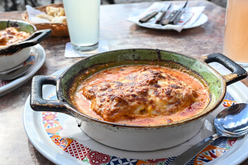 Lasagna, Italian pasta with ground beef, tomato sauce and mozzarella in a rustic ceramic casserole dish on a dining table in a restaurant, selected focus