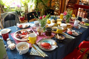 Large dining table, opulent and colorful setting with a lot of food like cheese, sausage and more for a festive informal meal with family or friends in a living room, selected focus
