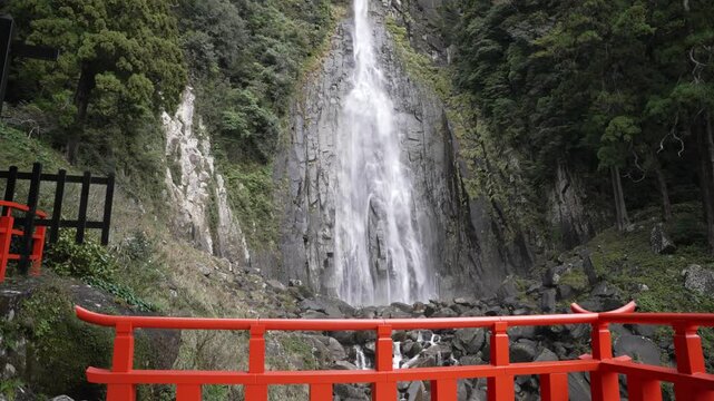 Scenic view of Nachi Falls plunging down a steep cliff face, framed by lush greenery and a traditional red bridge in Nachikatsuura, Japan