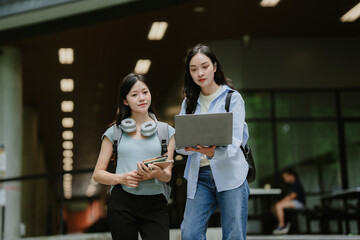 Two female college students are chatting and exchanging ideas about their studies on their laptops during their free time.