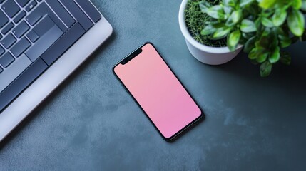 Modern smartphone with pink blank screen lying on textured gray desk alongside a keyboard and potted green plant, emphasizing technology and workspace setup