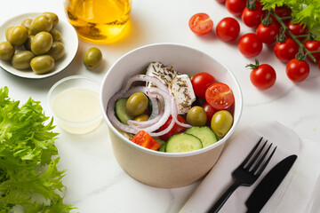 Greek salad of fresh cucumber, tomato, sweet pepper, red onion, feta cheese and olives with olive oil. Healthy take away food in cardboard box. Side view
