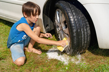 A boy in a blue T-shirt washes the front wheels with a sponge with foam.