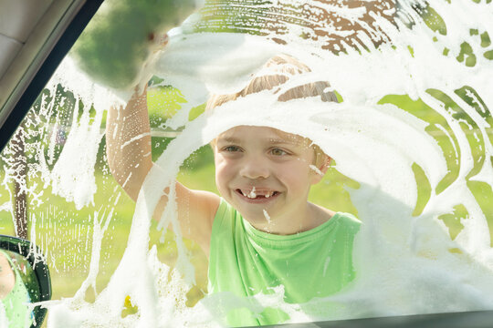 A boy in a green T-shirt looks out the window, which is covered in soap scum. He smiles a joyful smile.