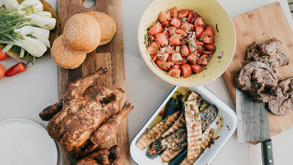 A table with a variety of food, including chicken, vegetables, and meat. The table is set for a meal, and the food looks delicious
