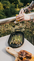 A man is preparing food on a grill, and he is adding lemon slices to the asparagus