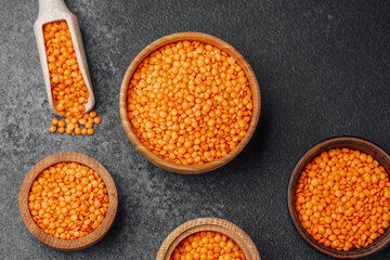 Bright orange lentils in wooden bowls on a dark stone surface
