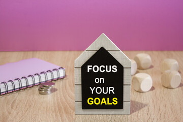 Focus on your goals symbol. Black board with words Focus on your goals on beautiful purple background. Notebook and silver coins on the table. Business concept.