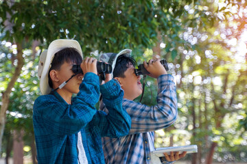 Two Asian boys use binoculars to study the local birds at school. Soft and selective focus.