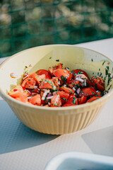 A bowl of tomatoes and onions is sitting on a table. The bowl is yellow and has a green border