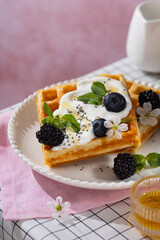 Belgian waffles with blueberries, honey and mint on a white plate. Breakfast with a cup of coffee and sweet waffles.