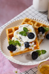 Belgian waffles with blueberries, honey and mint on a white plate. Breakfast with a cup of coffee and sweet waffles.