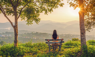 Rear view a girl sitting on a bench looking village mountain sunrise