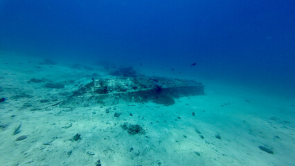 The hull of a sunken boat underwater. The overturned remains of a boat on a sandy sea bottom. A sunken boat on a deserted sea bottom in clear transparent water.