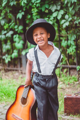 boy dressed in the style of the 20s laughs cheerfully and holds a guitar by the neck looking at the camera