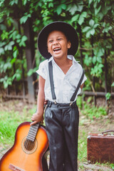 boy dressed in the style of the 20s laughs cheerfully and holds a guitar by the neck looking to the side