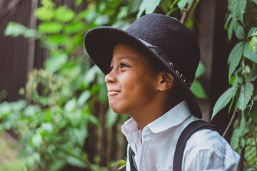 boy dressed in the style of the 20s stands by the hedge in profile