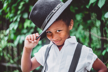boy dressed in the style of the 20s lifts his hat, holding it by the brim, looking at the camera from under his brows