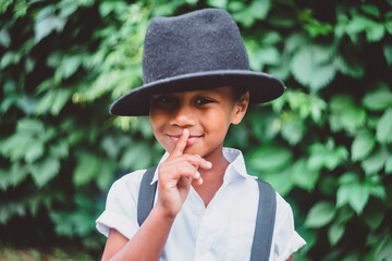 close-up of a boy in a hat in the style of the 20s, smiling, holding a finger to his mouth, a sign of silence and keeping a secret