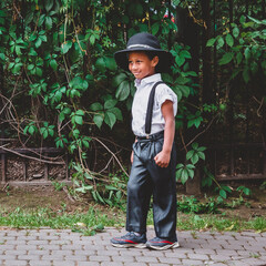 A boy dressed in the style of the 20s stands on the street in the summer smiling