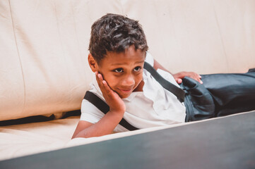 a boy dressed in the style of the 20s lies on a leather sofa resting his cheek with his palm