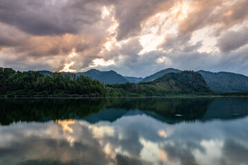 A serene scene at Almsee Lake, capturing the peaceful reflection of clouds and surrounding mountains in the still waters. 