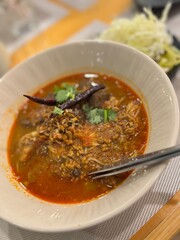 Authentic Northern Thai 'Khanom Jeen Nam Ngiao', a spicy and savory rice noodle soup with a rich, aromatic broth made from pork ribs, blood jelly, and tomatoes, garnished with crispy garlic and chili.