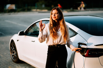 Business woman with red hair charges electric car at public charging station during daytime