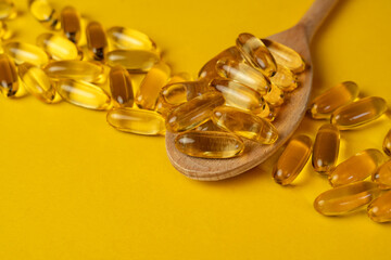 Wooden spoon with capsules, omega-3, omega-9 and scattered capsules next to each other on yellow background. Soft focus. Dietary supplements, vitamin D, vitamin E.