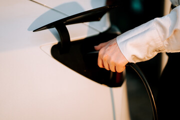 Business woman with red hair charges her electric car at a public charging station in the evening