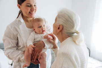 Mother, grandmother and little baby child on hands indoors