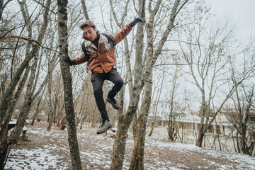 A person balances himself between tree branches in a snow-covered woodland, engaging in active play and adventure in cold weather.
