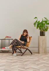 Fototapeta premium The image shows a woman comfortably seated in a woven chair, looking at a tablet. She is wearing casual indoor slippers, suggesting a relaxed home environment.