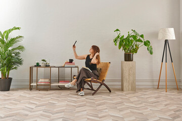 The image shows a woman comfortably seated in a woven chair, looking at a tablet. She is wearing casual indoor slippers, suggesting a relaxed home environment.